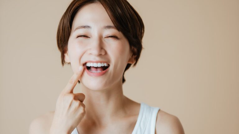 セラミック治療で白くきれいな歯になった歯を指さし嬉しそうな女性