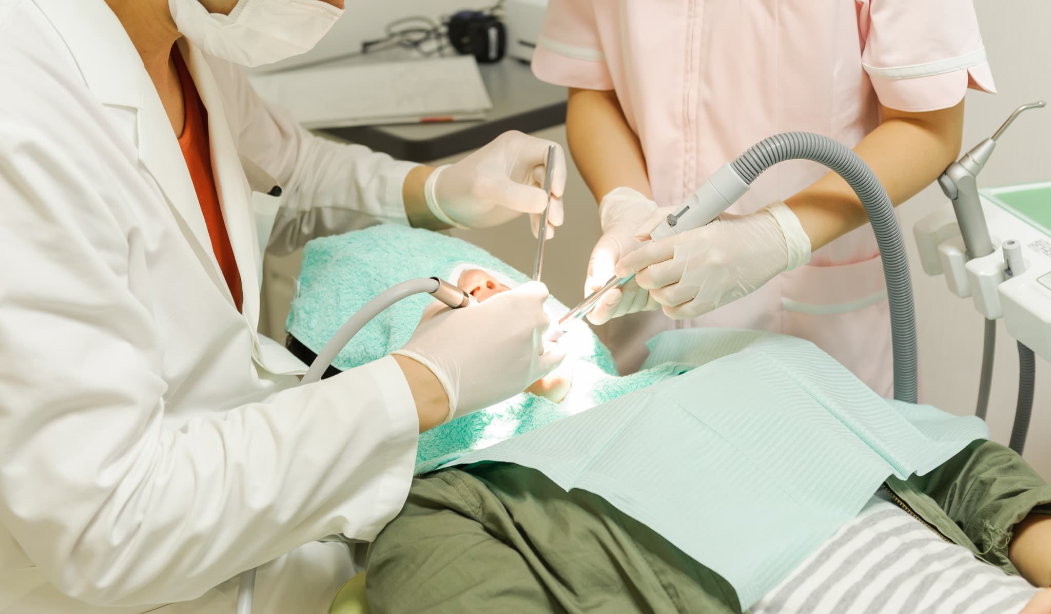 銀歯の下の虫歯治療を受けている患者と治療する歯科医師とアシスタントする歯科衛生士