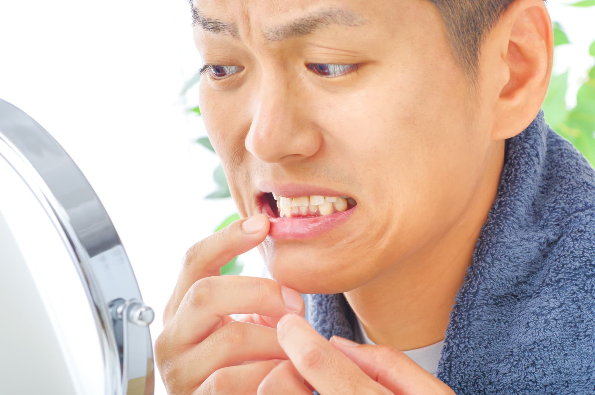 鏡で歯ぐきをチェックしながら眉間にしわを寄せる男性